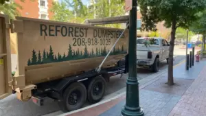 Reforest Dumpsters trailer parked on a downtown city street next to a pickup truck and storefronts